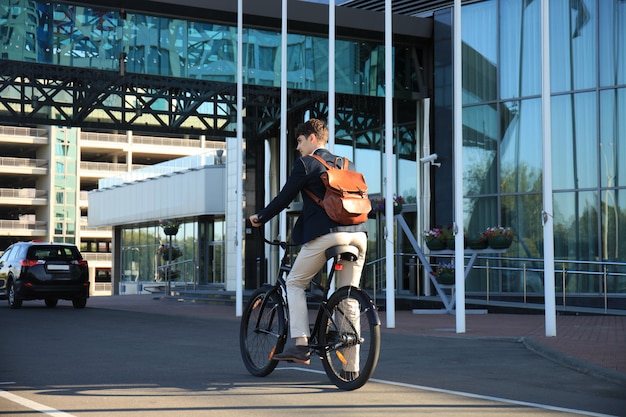 Jovem empresário confiante andando de bicicleta nas ruas da cidade.