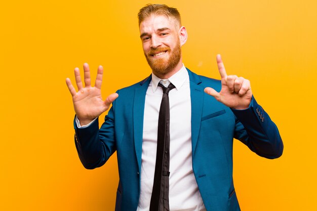 Jovem empresário de cabeça vermelha sorrindo e olhando amigável, mostrando o número sete ou sétimo com a mão para a frente, contando para baixo