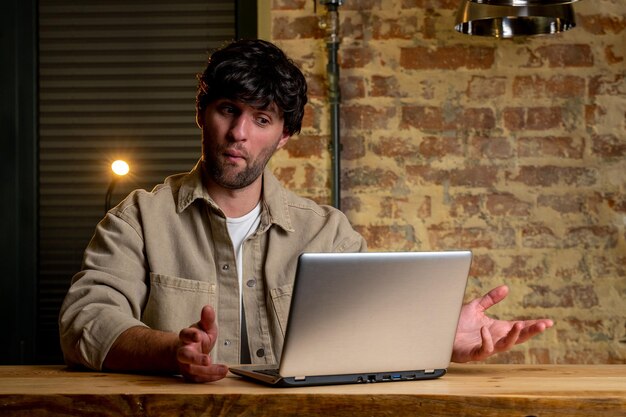 Jovem empresário de cabelos negros trabalhando com um laptop em uma mesa na sala de estar da casa felizmente surpreso