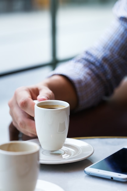 Jovem empresário de sucesso sentado em um café, bebendo café da manhã e usando o smartphone. Composição de estilo de vida com luz natural