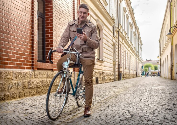 Foto jovem empresário elegante com seu smartphone fica na rua com bicicleta retro esportiva em um dia ensolarado