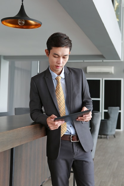 Jovem empresário em pé na mesa no local de trabalho no escritório usando o tablet