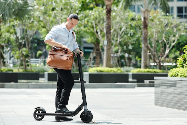 Jovem empresário em pé na scooter e verificando o documento em sua bolsa de couro