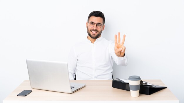 Jovem empresário em um local de trabalho feliz e contando três com os dedos