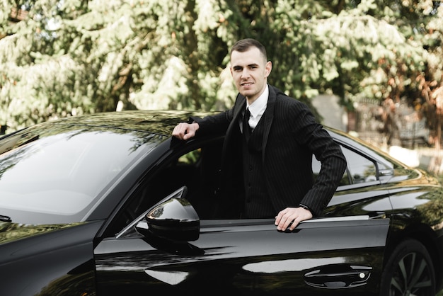 Jovem empresário está sentado em um carro caro e olhando para a câmera. o noivo está dirigindo. homem de negocios. cara de sucesso. homem rico.