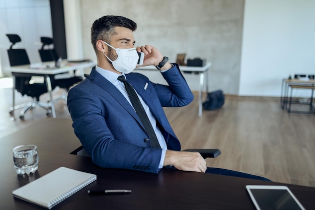 Jovem empresário falando ao telefone enquanto usava máscara facial no escritório