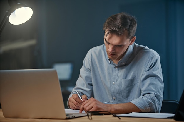 Jovem empresário fazendo anotações em seu caderno durante o trabalho noturno