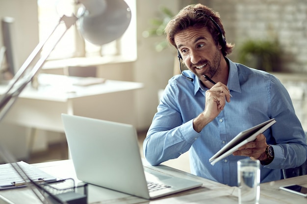 Jovem empresário feliz usando computador enquanto tem reunião on-line em seu escritório