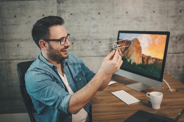 Jovem empresário freelance alegre bem sucedido está se divertindo e mostrando o pequeno modelo de avião, explicando como ele voa.