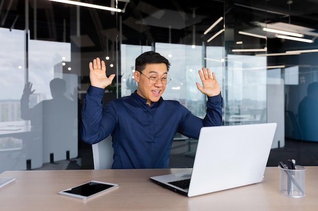 Jovem empresário freelancer asiático no escritório à mesa conversando por videochamada com