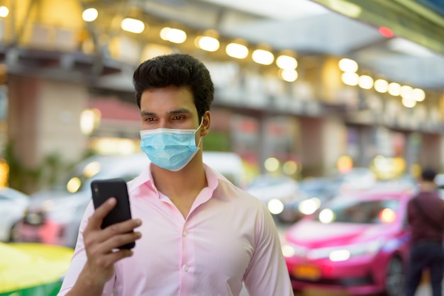 Jovem empresário indiano com máscara usando telefone nas ruas da cidade
