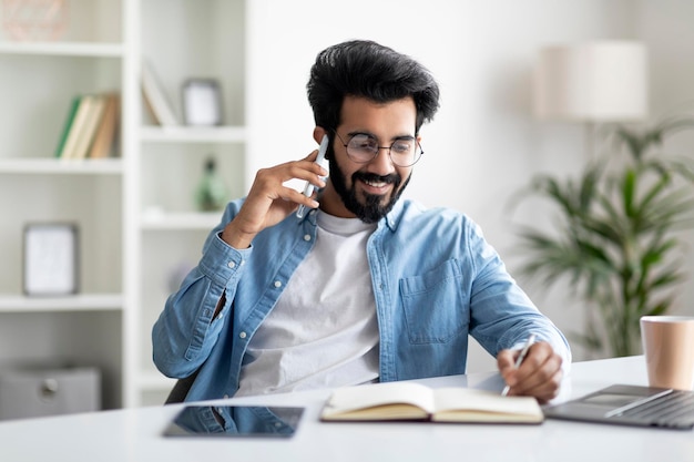 Jovem empresário indiano falando no celular e fazendo anotações no escritório