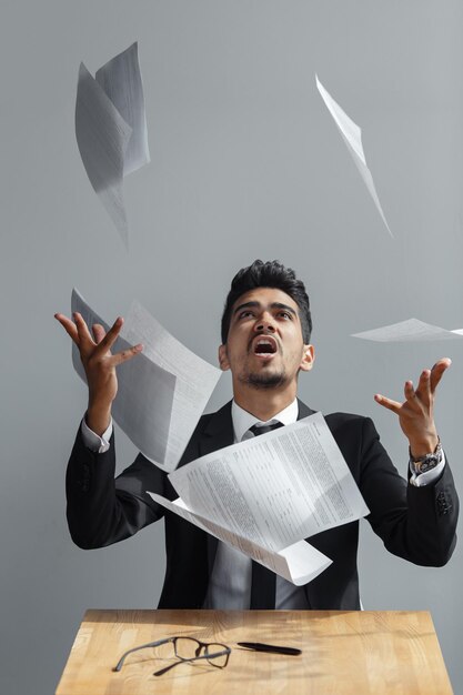 Foto jovem empresário jogando algumas folhas de papel no fundo cinza