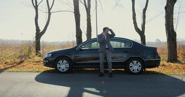 Jovem empresário, ligando para o serviço de carro na assistência rodoviária após o carro quebrado. Carro quebrado, conceito de avaria do carro.