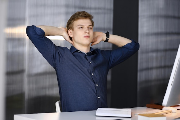 Jovem empresário loiro e programador esticando as mãos depois de trabalhar duro com o computador. Negócio de inicialização leva ao sucesso.