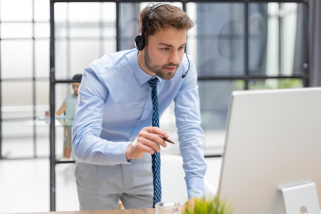 Jovem empresário moderno analisando dados usando o computador enquanto trabalhava no escritório com colegas no fundo