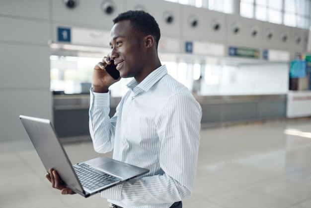 Jovem empresário negro com laptop e telefone negocia no showroom de carros. homem de negócios de sucesso em salão automóvel, homem negro com roupa formal