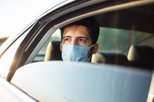 Jovem empresário pega um táxi e olha pela janela do carro usando máscara médica estéril. conceito de distância social.