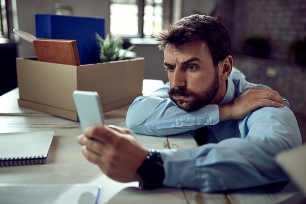 Jovem empresário perturbado usando telefone inteligente depois de perder o emprego no escritório