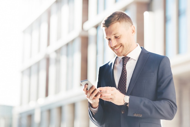 Jovem empresário próspero conversa on-line ou lê informações via telefone celular