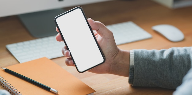 jovem empresário segurando o smartphone de tela em branco enquanto trabalhava em seu projeto