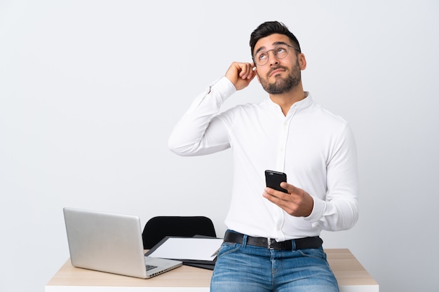 Jovem empresário segurando um telefone móvel com dúvidas com confundir a expressão do rosto