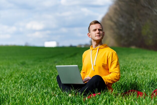 Jovem empresário sentado na grama verde, falando ao telefone e usando um computador laptop. Homem bonito, trabalhando com um computador em um parque em um dia ensolarado de verão. Conceito de trabalho freelance