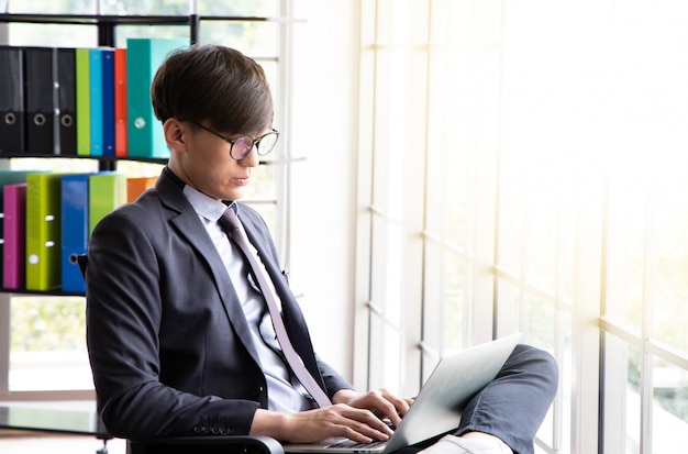 Jovem empresário sentar e trabalhar no escritório, ele colocou o laptop na perna.