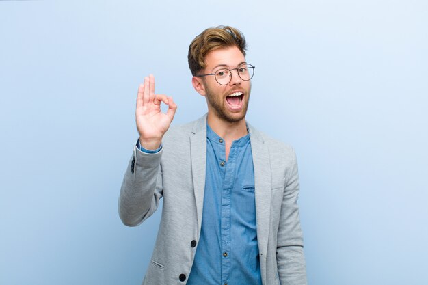 Jovem empresário, sentindo-se bem-sucedido e satisfeito, sorrindo com a boca aberta, fazendo sinal bem com a mão