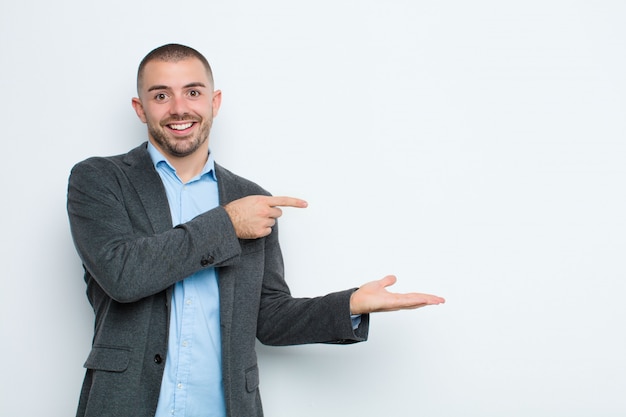 Jovem empresário sorrindo, sentindo-se feliz, despreocupado e satisfeito, apontando para o conceito ou ideia no espaço da cópia na lateral na parede plana