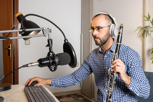 Jovem empresário tocando clarinete em casa e gravando música para transmitir online com seu computador