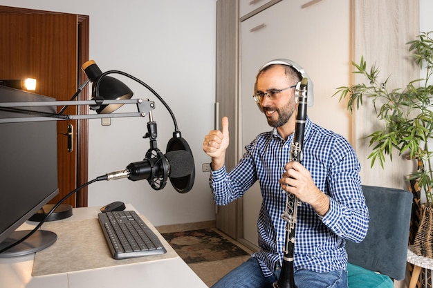 Jovem empresário tocando clarinete em casa e gravando música para transmitir online com seu computador