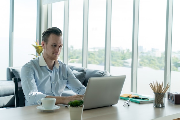 Foto jovem empresário trabalhando com laptop notebook sentado à mesa na sala de estar