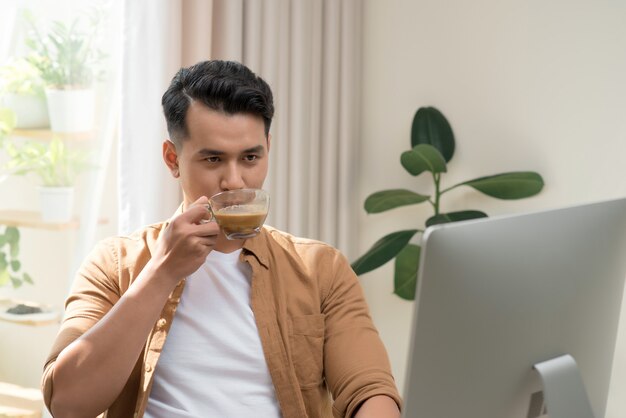 Jovem empresário trabalhando com Pc, tomando café no interior moderno do escritório branco. Homem bonito, funcionário de sucesso no trabalho com o computador.