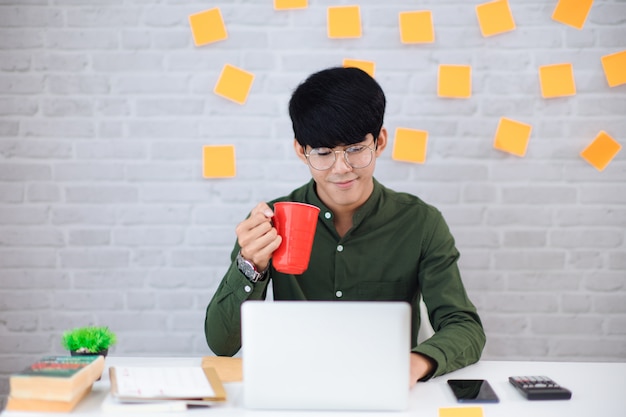 Foto jovem empresário trabalhando em casa e tomando café. ele olha para o laptop. foco e tom suave e suave