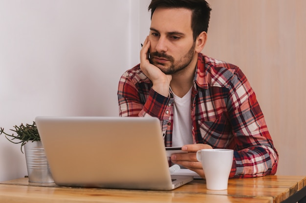 Jovem empresário trabalhando no escritório, sentado na mesa e olhando para a tela do computador portátil