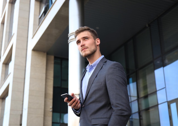 Jovem empresário urbano profissional em smartphone, andando na rua usando telefone celular.