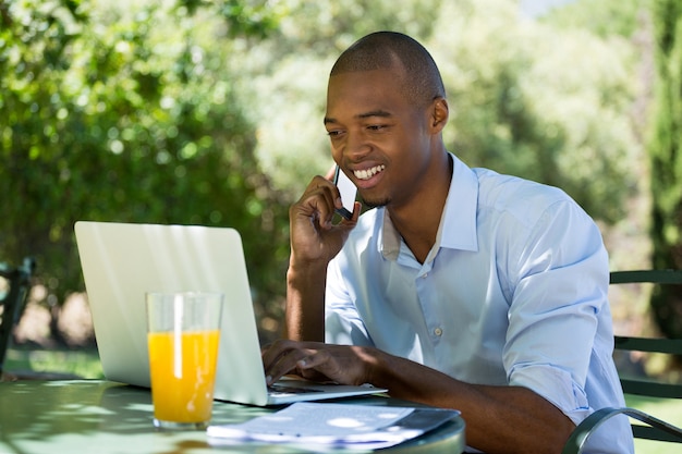 Jovem empresário usando laptop e telefone inteligente em restaurante ao ar livre