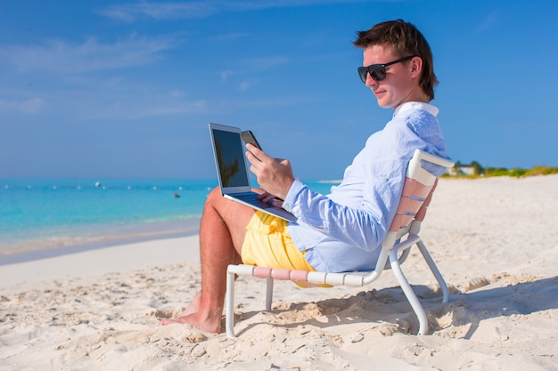 Jovem empresário usando laptop e telefone na praia tropical