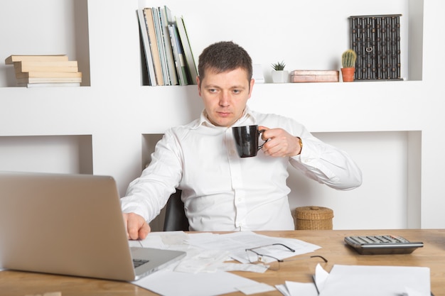 Jovem empresário usando o laptop em casa. Jovem trabalhando no computador em sua casa. Ele está tomando café