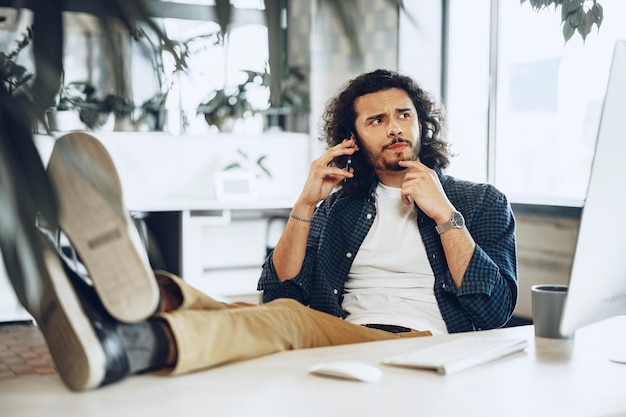 Jovem empresário vestido de maneira casual usando o celular no escritório