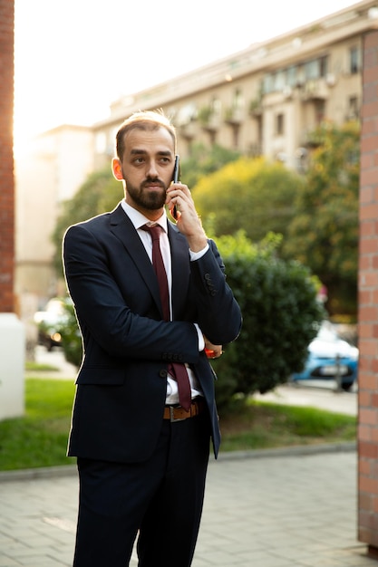 Jovem empresário vestido de terno fala no celular na rua. pôr do sol e fundo da rua