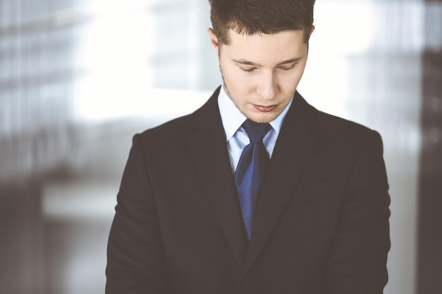 Jovem empresário vestindo terno e gravata, em pé no escritório. Conceito de sucesso empresarial hoje em dia.