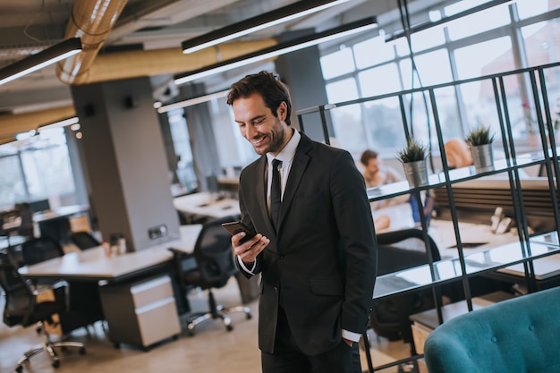 Jovem empresário vestindo terno preto usando smartphone moderno no escritório