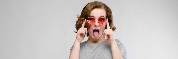 Jovem encantadora em uma camiseta cinza sobre um fundo cinza. Garota feliz em óculos vermelhos