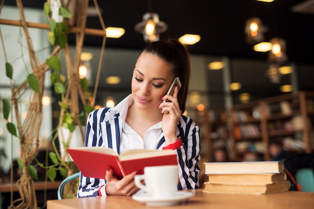 Jovem encantadora está falando no celular enquanto segura um livro.