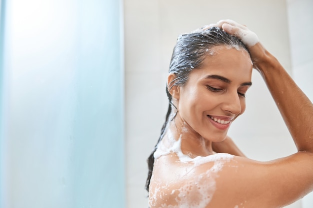 Jovem encantadora lavando o cabelo no chuveiro