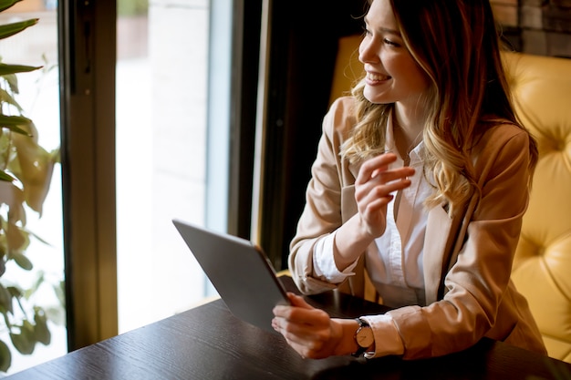 Jovem encantadora sorridente com tablet digital no café