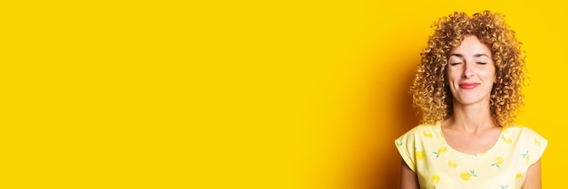 Foto jovem encaracolada sorrindo com os olhos fechados no banner de fundo amarelo