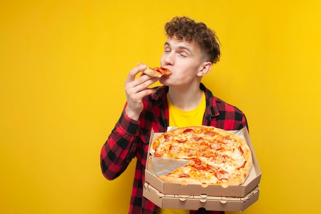 Jovem encaracolado comendo pizza em fundo amarelo estudante faminto gosta de fast food